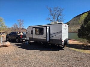 A scenic daytime camping setup with a caravan and truck by a lake in a natural setting.